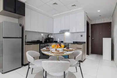 a kitchen with a table and chairs and a refrigerator at Stylish 1BR Apartment Near Silicon Mall & Airport in Dubai
