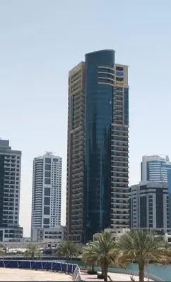 a tall building with palm trees in front of a city at Marina 1 Bedroom appartment in Dubai