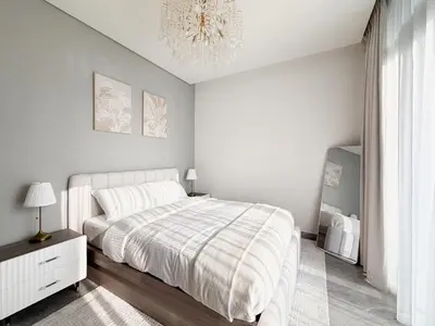 a white bedroom with a bed and a chandelier at 1BR - Peninsula One in Dubai