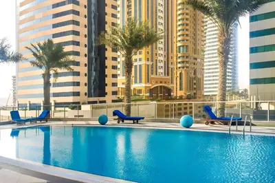 a swimming pool with chairs and palm trees and buildings at 2BR, Seaside Serenity, Sea View - Torch Tower, Dubai Marina by Deluxe Holiday Homes in Dubai