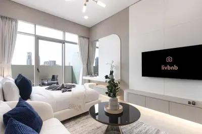 a living room with a bed and a tv on a wall at Elegant Designer Studio with Balcony & Rooftop Pool in JVC in Dubai