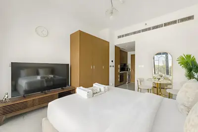 a white bedroom with a large tv and a bed at Elegant Retreat Studio in Azizi Mirage in Dubai