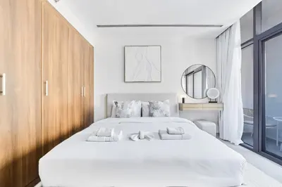 a white bedroom with a large bed and a mirror at Elegant 1BR Apartment in Ikarus, Dubai Production City in Dubai