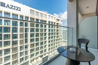 a glass table and chairs on a balcony with a building at Open layout Studio with Balcony - Azizi Riviera 67, Al Merkadh by Deluxe Holiday Homes in Dubai