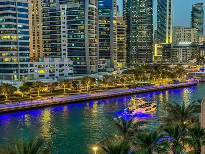 a boat in a river in a city at night at Marina Elegance, Walk to JBR Beach and Ain Dubai w Stunning Canal View in Dubai