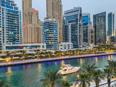 a boat in a river in a city with tall buildings at Marina Elegance, Walk to JBR Beach and Ain Dubai w Stunning Canal View in Dubai
