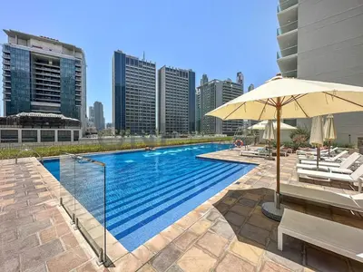 a swimming pool with an umbrella and some buildings at Modern 2BR I DAMAC Reva Residences I Canal Views in Dubai