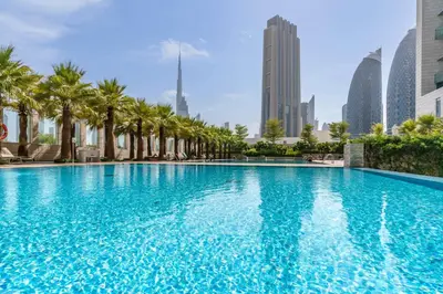 a large swimming pool with palm trees and buildings at Silkhaus Studio Burj Daman with Burj Khalifa View in Dubai