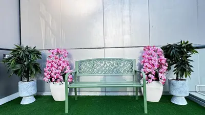a green bench and two potted plants with flowers at 1 Bedroom centrally located with large balcony in Dubai