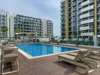 a large swimming pool with chairs and buildings at Chic Studio at Azizi Riviera Near Downtown Dubai in Dubai