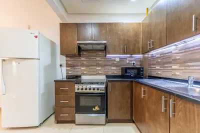 a kitchen with wooden cabinets and a white refrigerator at HAVN - Studio in Botanica, JVC in Dubai