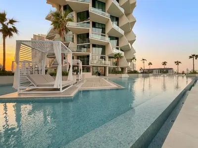 a resort swimming pool with a hotel in the background at Luxe 1BR in JVC with Private Jacuzzi & Pool Access in Dubai