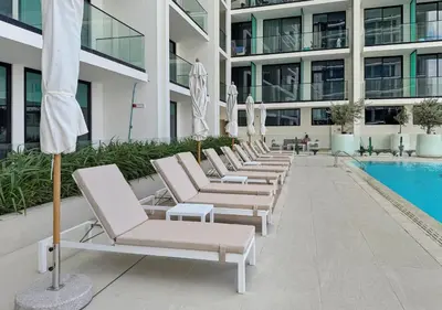 a row of chaise lounge chairs next to a swimming pool at Stylish JVC Studio Hotel-Style Comfort in Dubai