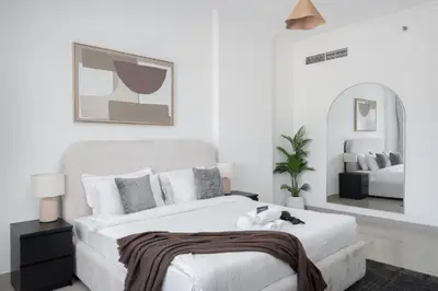 a white bedroom with a large white bed and a mirror at StayShort - Modern JVC 1 bed Sleeps 4 with Swimming Pool in Dubai