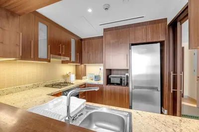 a kitchen with wooden cabinets and a stainless steel refrigerator at Waves - Luxury 2BR Apt With Burj Khalifa & Fountain View in Dubai