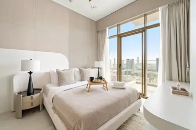 a white bedroom with a bed and a large window at VayK - Bright Modern Apartment in JVC - 1BR Gem in Dubai