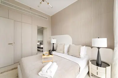 a white bedroom with a large white bed and a table at VayK - Bright Modern Apartment in JVC - 1BR Gem in Dubai