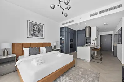 a bedroom with a large white bed and a kitchen at VayK - Ideal Studio in Sobha Hartland in Dubai