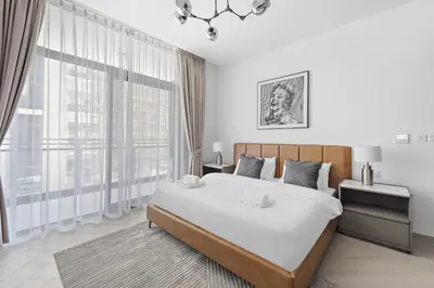 a white bedroom with a large bed and large windows at VayK - Ideal Studio in Sobha Hartland in Dubai