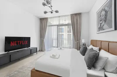 a white bedroom with a bed and a tv at VayK - Ideal Studio in Sobha Hartland in Dubai
