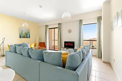 a living room with a blue couch and a tv at VayK - Light-Filled and Spacious 1BR in JBR in Dubai