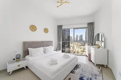 a white bedroom with a large white bed and a window at VayK - Generous 2BR Offering Burj Khalifa Views in Dubai