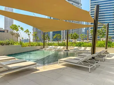 a pool with lounge chairs and a large yellow umbrella at VayK - Sunlit Studio with Canal Views in Business Bay in Dubai