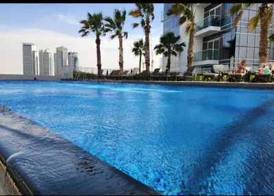 a large swimming pool with palm trees and a building at Modern Luxury Studio Damac Hills With Golf View in Dubai