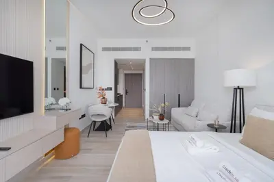 a white living room with a couch and a tv at Chic Pool-View Studio Oxford Gardens by Czechin in Dubai