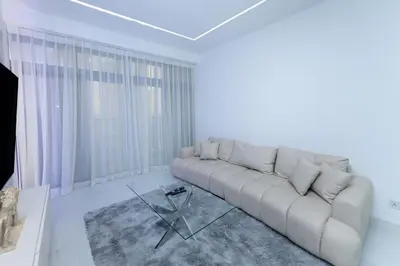 a white living room with a couch and a glass table at Escape 24 Spacious 1BR Lake View, Global Lake View, JLT in Dubai