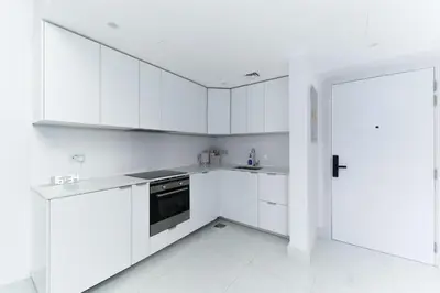 a white kitchen with white cabinets and a door at Escape 24 Spacious 1BR Lake View, Global Lake View, JLT in Dubai