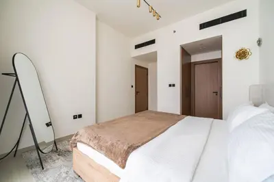 a white bedroom with a bed and a mirror at SettlerHomes - JVC Skyline Views - Pool & Gym in Dubai