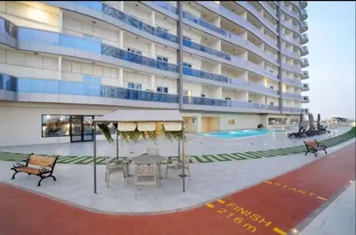 a large building with a table and chairs and a pool at Vogue Sports City Hera Tower Near First Avenue Mall, Studio Apartment with Balcony, Canal and City View, Access to all Amenities in Dubai