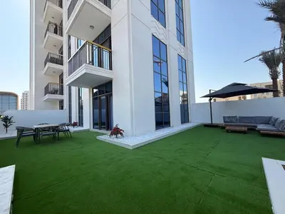 an apartment patio with a green lawn in front of a building at Italian-Design 2BR l Large Private Terrace l Ground Floor in Dubai