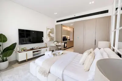 a white bedroom with a large bed and a living room at Contemporary Studio with Premium Design in JVC in Dubai