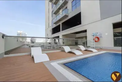 a balcony with a pool and white chairs and a building at Vogue JVC Jeewar Tower near Circle Mall, One Bedroom Apartment with Balcony and City View, Access to all Amenities in Dubai