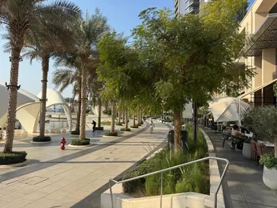 a sidewalk with palm trees and people sitting on benches at Vacationer l Contemporary 2 Bedroom l Pool, Gym, Private Beach Access in Dubai