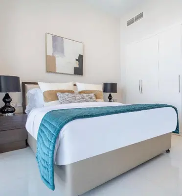 a white bedroom with a large bed and two lamps at Luxury Living in JVC 1BR Apartment in Dubai