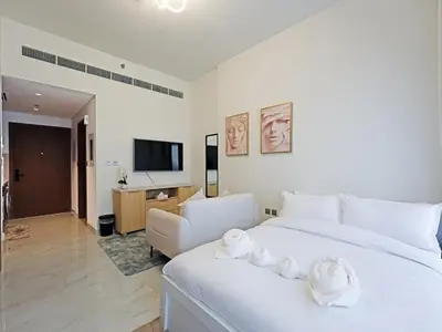 a bedroom with a large white bed and a living room at Elegant Modern Studio- Peaceful Studio City in Dubai