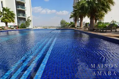 a blue swimming pool with palm trees and buildings at Modern Luxury Studio Damac Hills With Golf View in Dubai