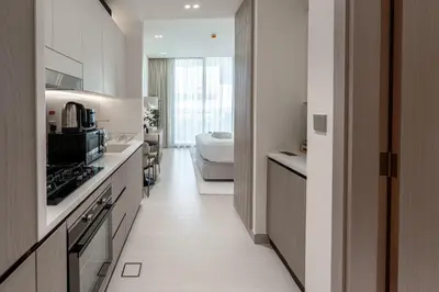 a kitchen with white cabinets and a bed in a room at Modern and Serene Studio - JVC in Dubai