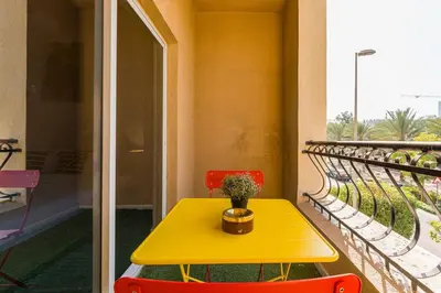 a yellow table and two red chairs on a balcony at Chic Studio Near Circle Mall & Dubai Sports City in Dubai