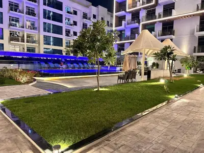 a lawn in front of a building at night at Pool view Studio with balcony in Arjan in Dubai