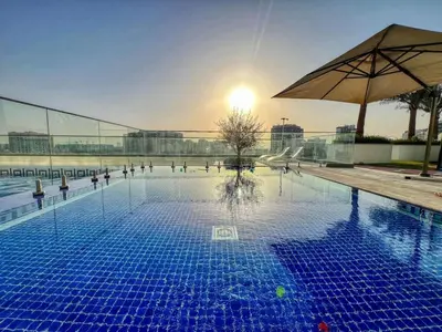 a large swimming pool with an umbrella and the sun at Classy Studio ideal for long stays with balcony in Dubai