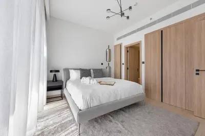 a white bedroom with a bed and a wooden cabinet at Modern Apartment w/ Balcony & Rooftop Amenities in Dubai