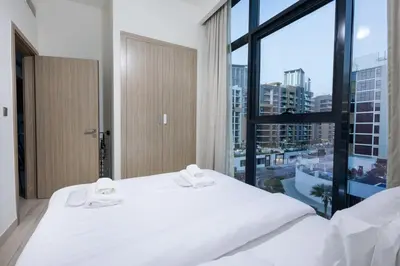 a white bed in a room with a large window at Cozy 1BR with Pool & Gym l 15mn to Downtown in Dubai