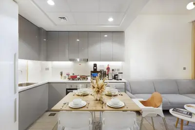 a kitchen and living room with a table and chairs at Cozy 1BR with Pool & Gym l 15mn to Downtown in Dubai