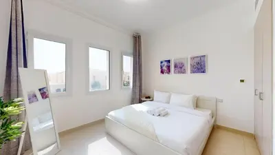 a white bedroom with a white bed and windows at Vacationer l Serene 2 Bed Villa l Lush Garden l Family Friendly in Nadd Shubayḩ