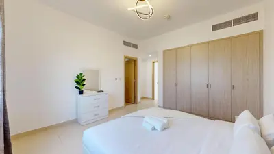 a bedroom with a white bed and a wooden cabinet at Vacationer l Serene 2 Bed Villa l Lush Garden l Family Friendly in Nadd Shubayḩ