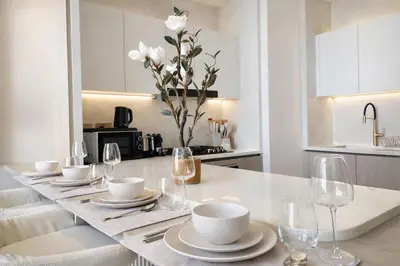 a white kitchen with a table with plates and wine glasses at Binghatti Royale Luxe 1BR W Private Pool Parking in Dubai
